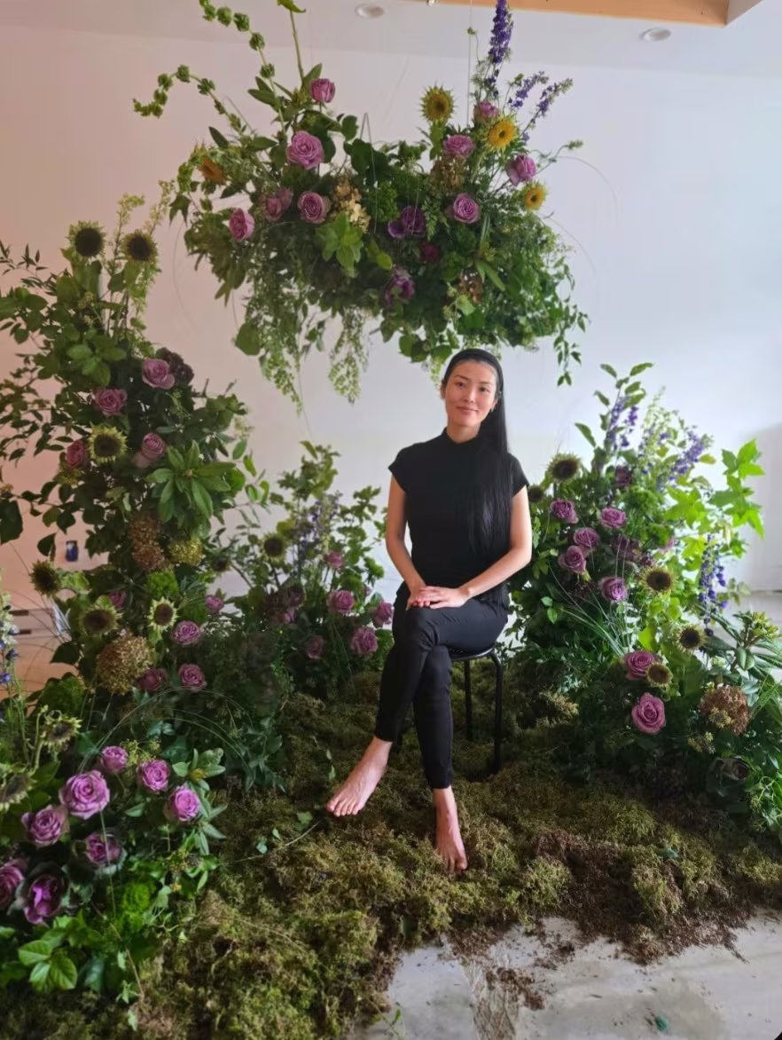 Seated beneath a hanging ceremony installation in a moss meadow