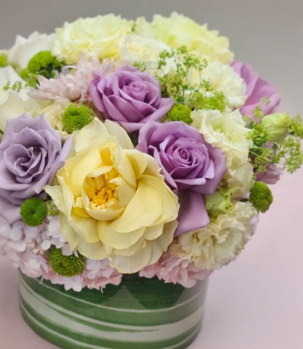 Packed vase arrangement of pastel roses and hydrangeas in a green glass vase